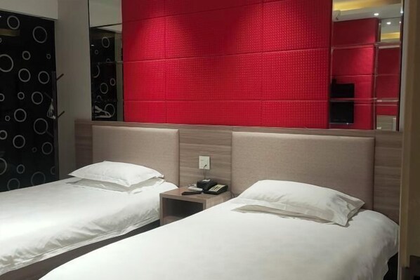 A hotel room with two single beds, a red accent wall, and a mirror reflecting the room.