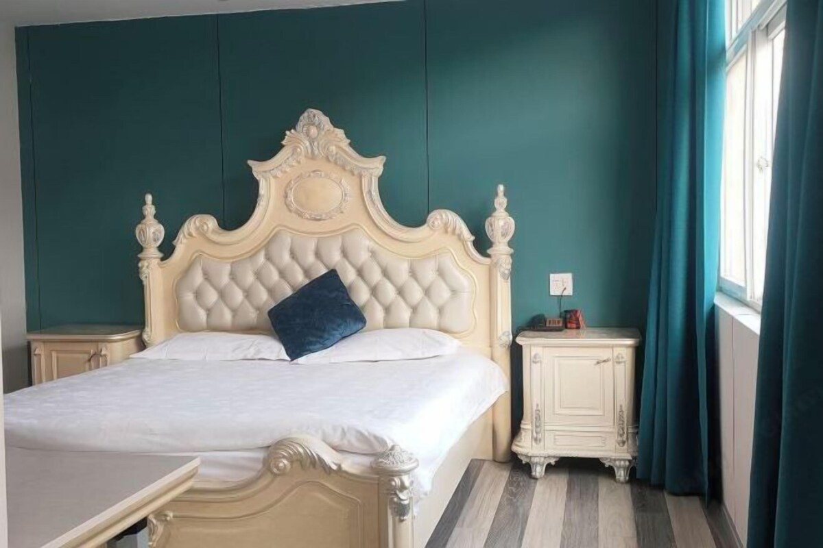 Quarto com uma cama grande, mesa de cabeceira, cômoda e janela com cortinas.
