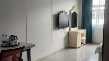 A hotel room with a bed, a desk with a chair, a television, a dresser, and a window with curtains.
