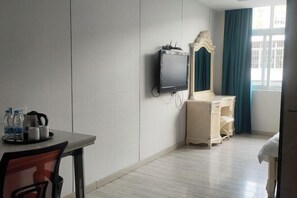 A hotel room with a bed, a desk with a chair, a television, a dresser, and a window with curtains. - Margarita Boutique Hotel (Guangde)