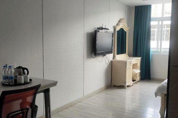 Quarto de hotel com cama, escrivaninha com cadeira, televisão, cômoda e janela com cortinas.