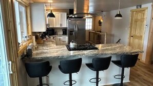 Een moderne keuken met een centraal eiland, barstoelen en een roestvrijstalen koelkast.