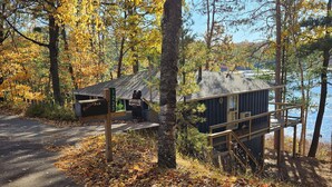 Een vakantiehuisje met een brievenbus en een beeldhouwwerk van een beer, omringd door herfstbladeren en bomen.