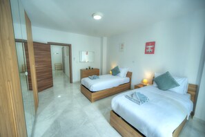 Habitación de hotel con dos camas, un armario de madera, un espejo, una mesita de noche con lámpara y un aplique de pared.