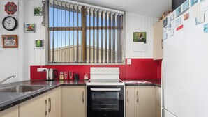 A kitchen with a stove, oven, sink, and window with bars. There are various kitchen items and decorations on the walls.