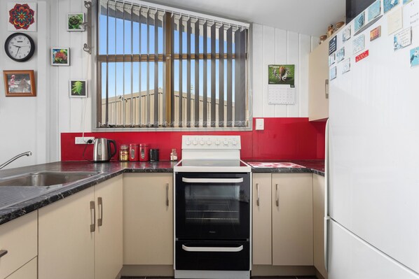 A kitchen with a stove, oven, sink, and window with bars. There are various kitchen items and decorations on the walls.
