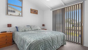A bedroom with a bed, a dresser, a nightstand, a window with blinds, and a view of the outside.