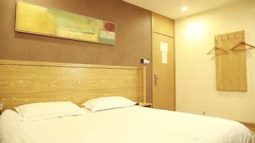 Quarto de hotel com cabeceira de madeira, cama com roupa de cama branca, um quadro na parede e um cabideiro.