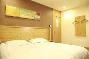 A hotel room with a wooden headboard, a bed with white bedding, a painting on the wall, and a coat rack. - Jiangwen Hotel (Shanghai)