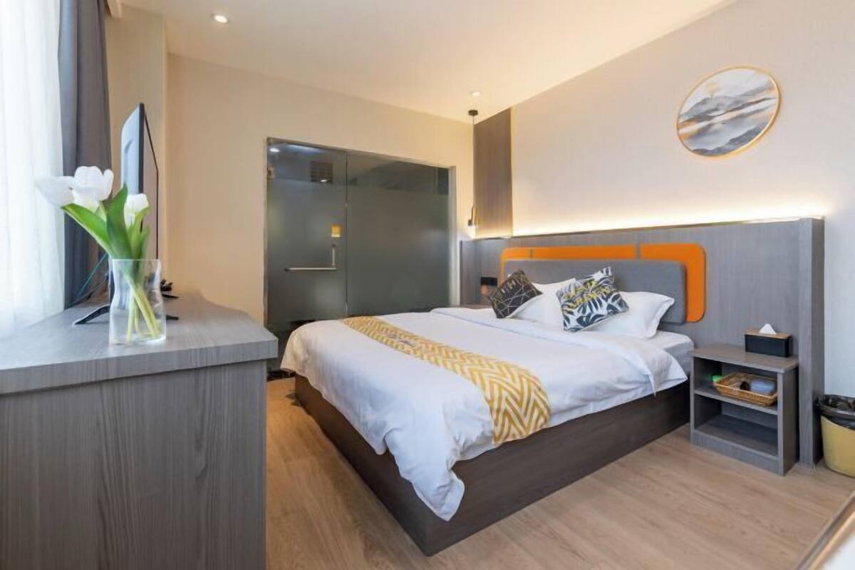 A modern hotel room with a bed, bedside tables, a desk, and a vase of flowers.
