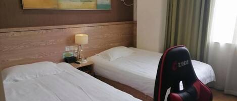Habitación de hotel con dos camas, un escritorio con lámpara, una silla gamer roja y un cuadro en la pared.