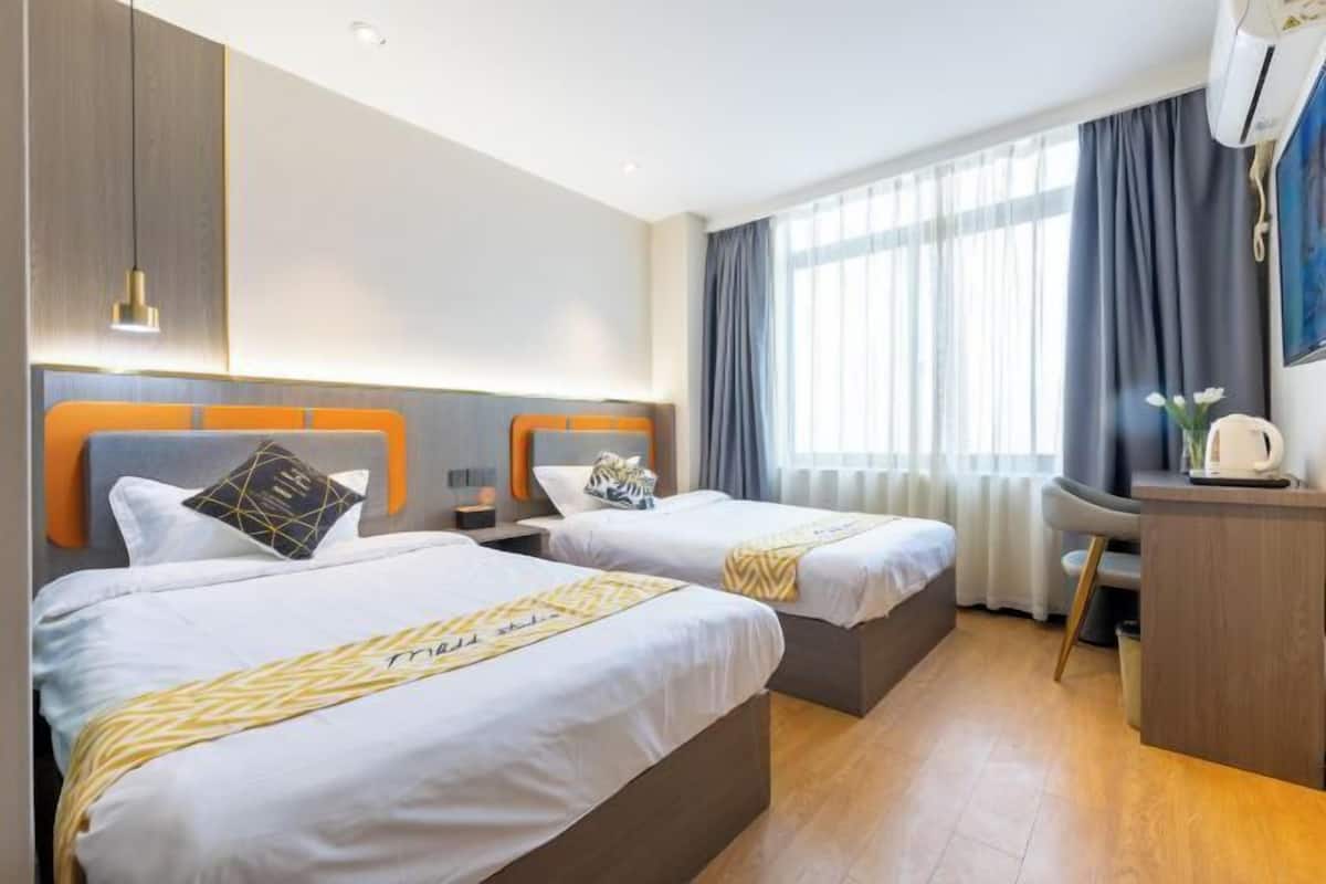 A hotel room with two beds, a desk, a chair, and a window with curtains.