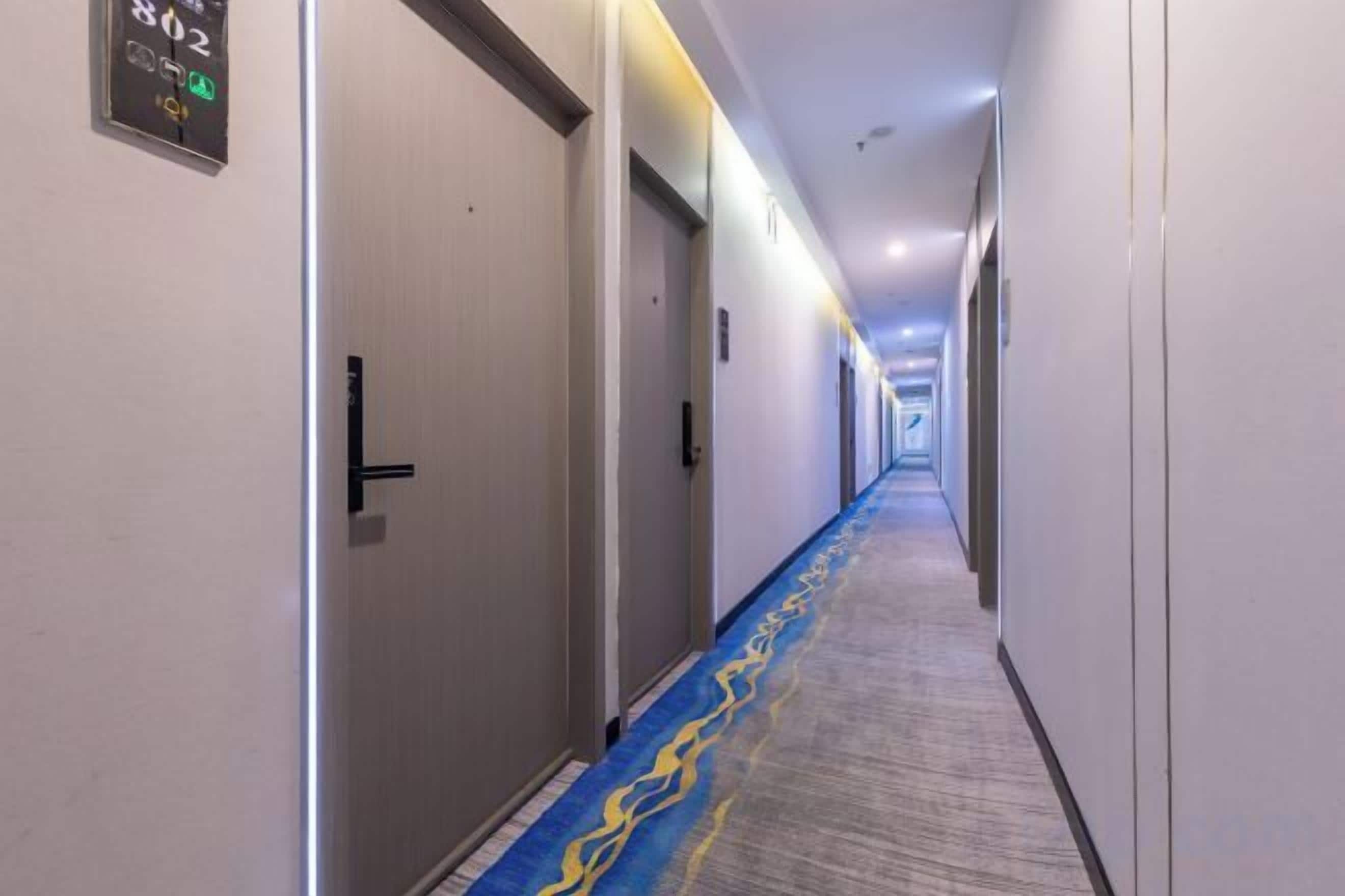 A hotel corridor with doors, carpeted flooring, and overhead lighting.