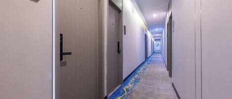 A hotel corridor with doors, carpeted flooring, and overhead lighting.