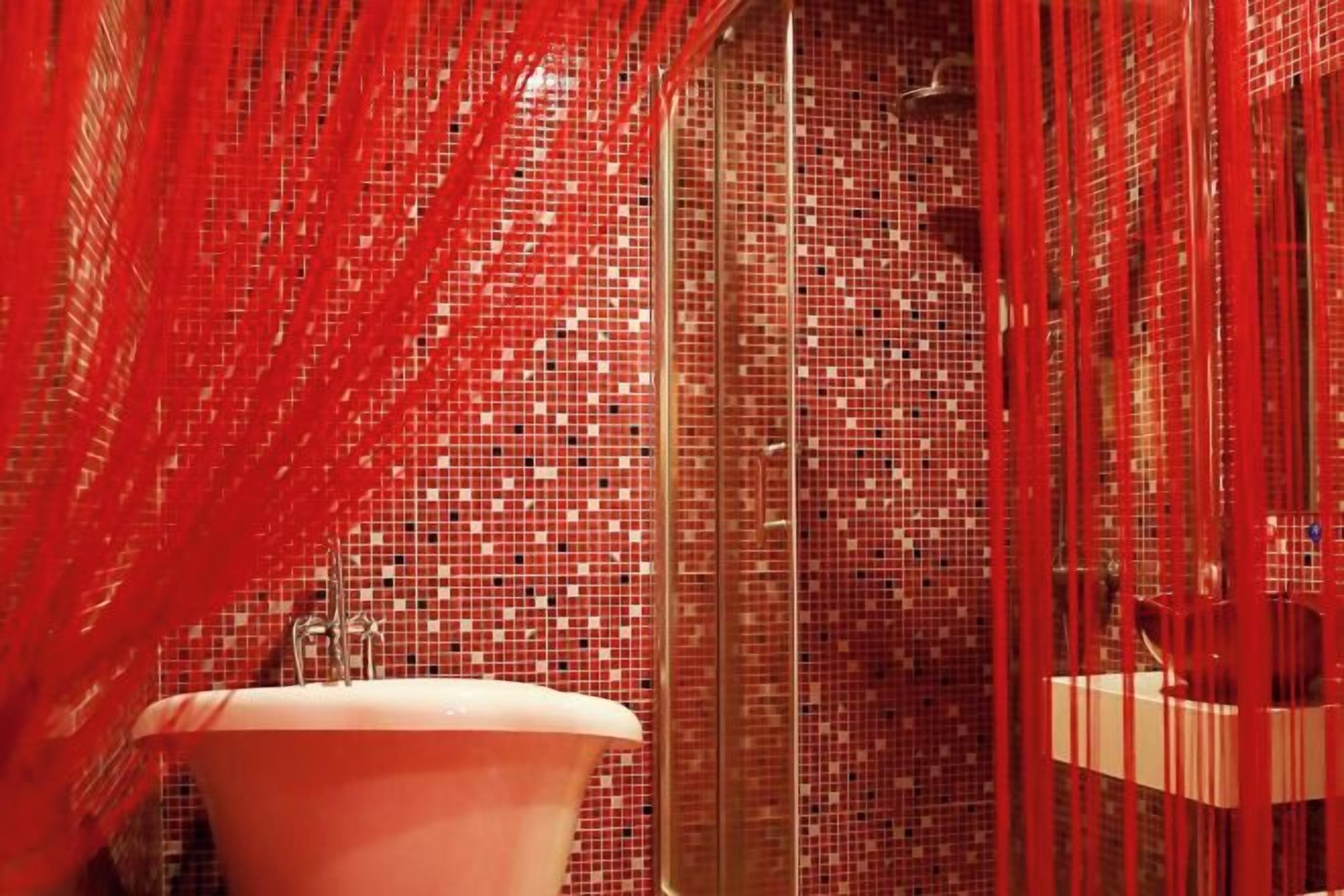 Um banheiro com pia rosa, paredes azulejadas e cortinas vermelhas.