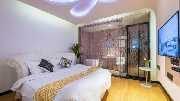 Une chambre moderne avec un grand lit, une cloison en verre et une petite table sur laquelle est posé un vase.