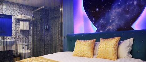 A bedroom with a large bed, a starry wall mural, and a shower area.