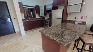 A kitchen with granite countertops, stainless steel appliances, and dark wooden cabinets. - Ocean view 2nd floor, luxury 1 bedroom condo at EL FARO by DPM (Playa del Carmen)