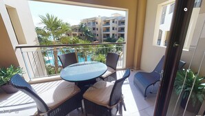 A balcony with a glass table and wicker chairs, overlooking a pool and buildings. - Ocean view 2nd floor, luxury 1 bedroom condo at EL FARO by DPM (Playa del Carmen)