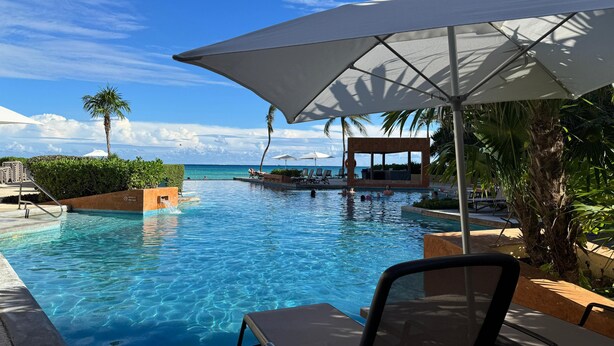 A poolside area with lounge chairs and umbrellas, a clear view of the ocean, and a wooden deck. - Ocean view 2nd floor, luxury 1 bedroom condo at EL FARO by DPM (Playa del Carmen)