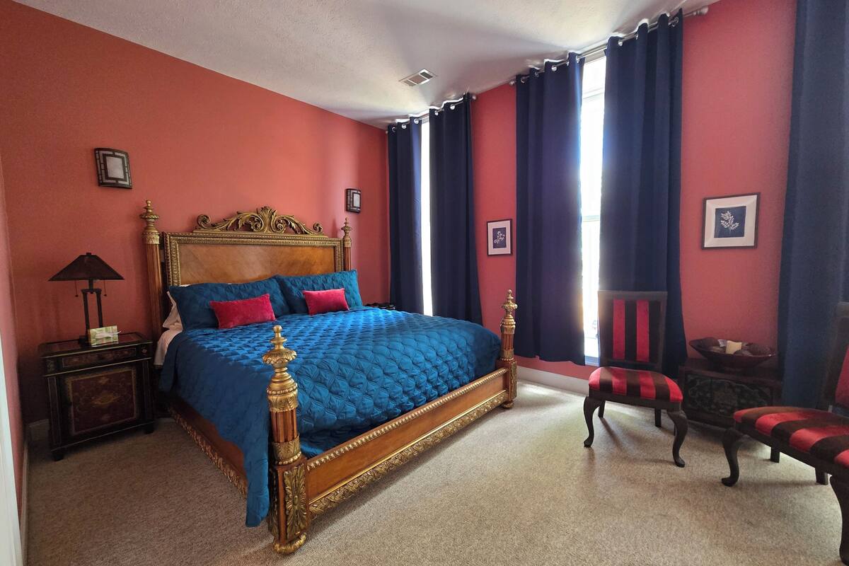 A bedroom with a large bed, a nightstand, a chair, and a window with curtains.