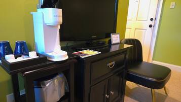 A hotel room with a black desk, a coffee machine, a television, and a black leather chair.