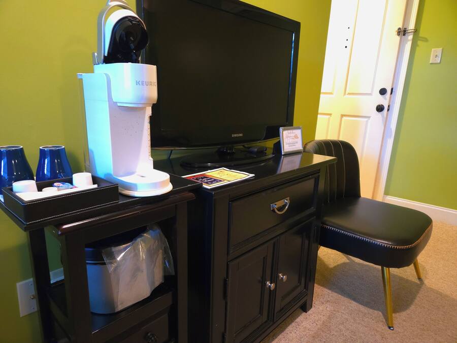 A hotel room with a black desk, a coffee machine, a television, and a black leather chair.