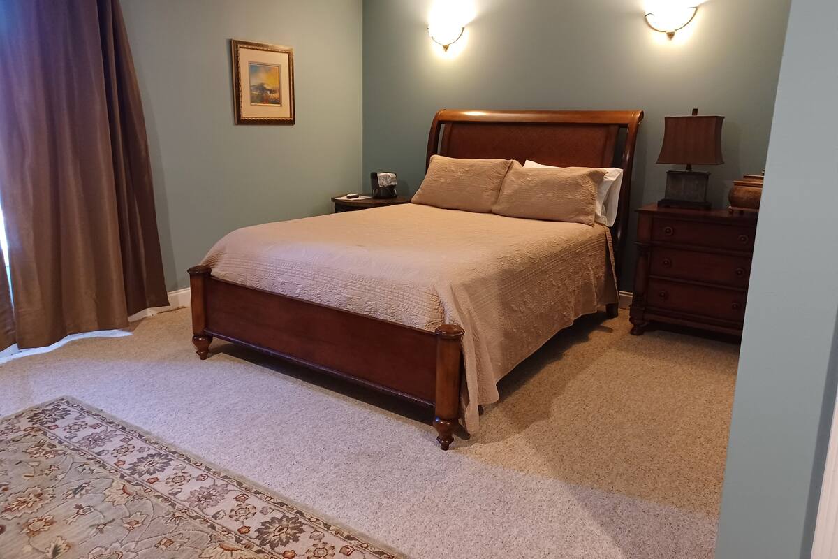 A bedroom with a large bed, a nightstand, a dresser, and a wall-mounted lamp.