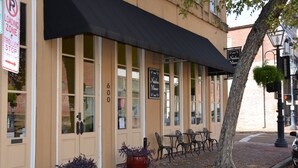A building with a black awning, a sign reading "Nathans Manor," and a number "600" on the door. There are outdoor tables and chairs, and a tree is visible. - Natchez Manor Bed & Breakfast (Natchez)