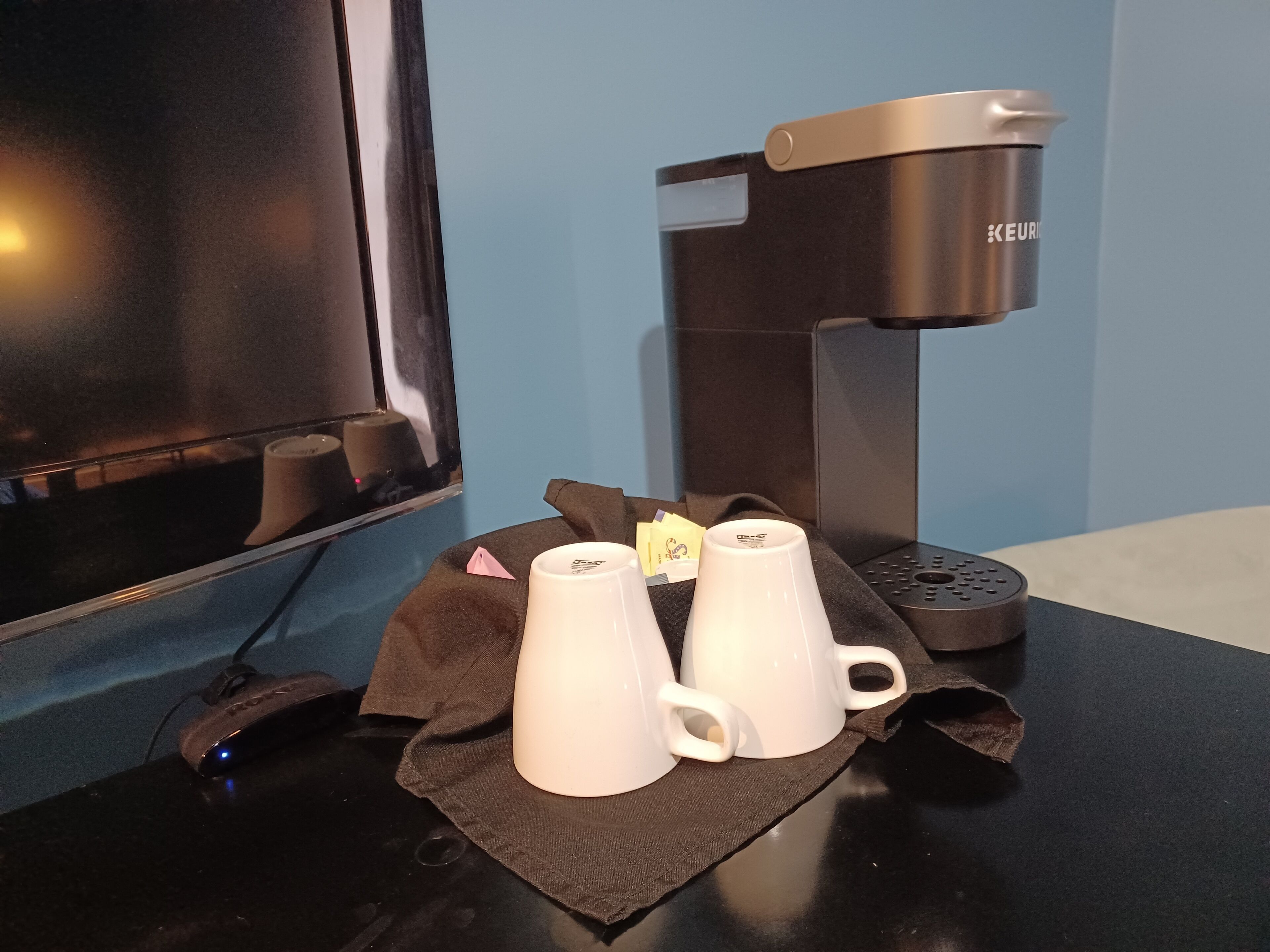 A coffee machine, two white cups, and a brown cloth on a table.