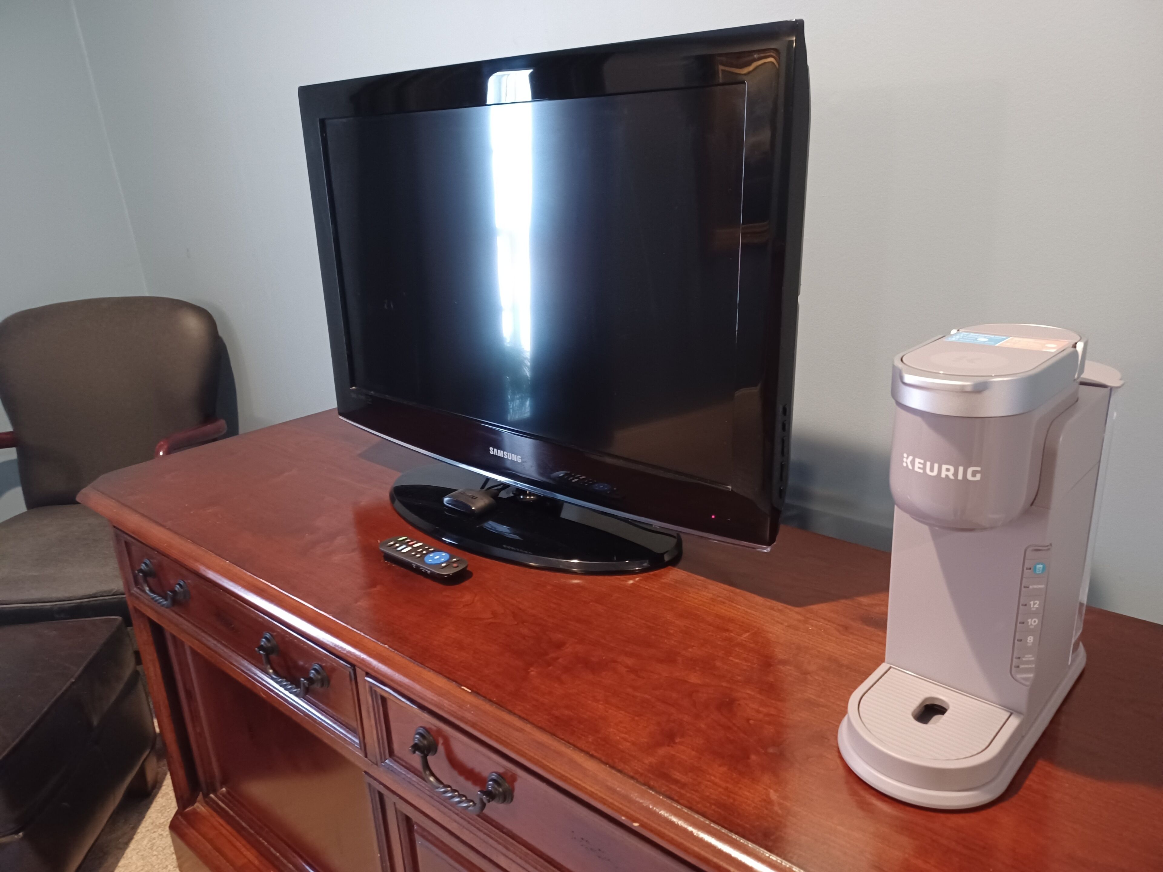 A Samsung TV on a wooden cabinet, a Keurig coffee maker, and a remote control.