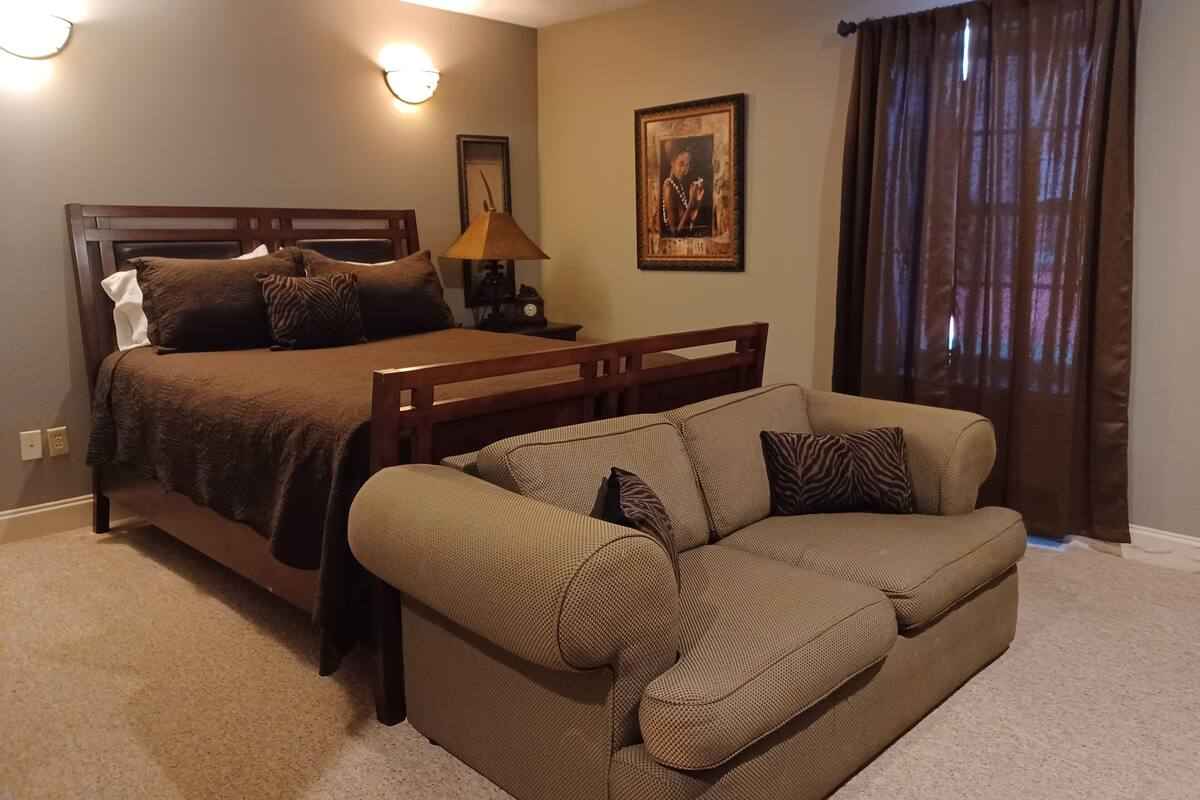 A bedroom with a bed, a nightstand, a lamp, a framed picture, and a window with curtains.