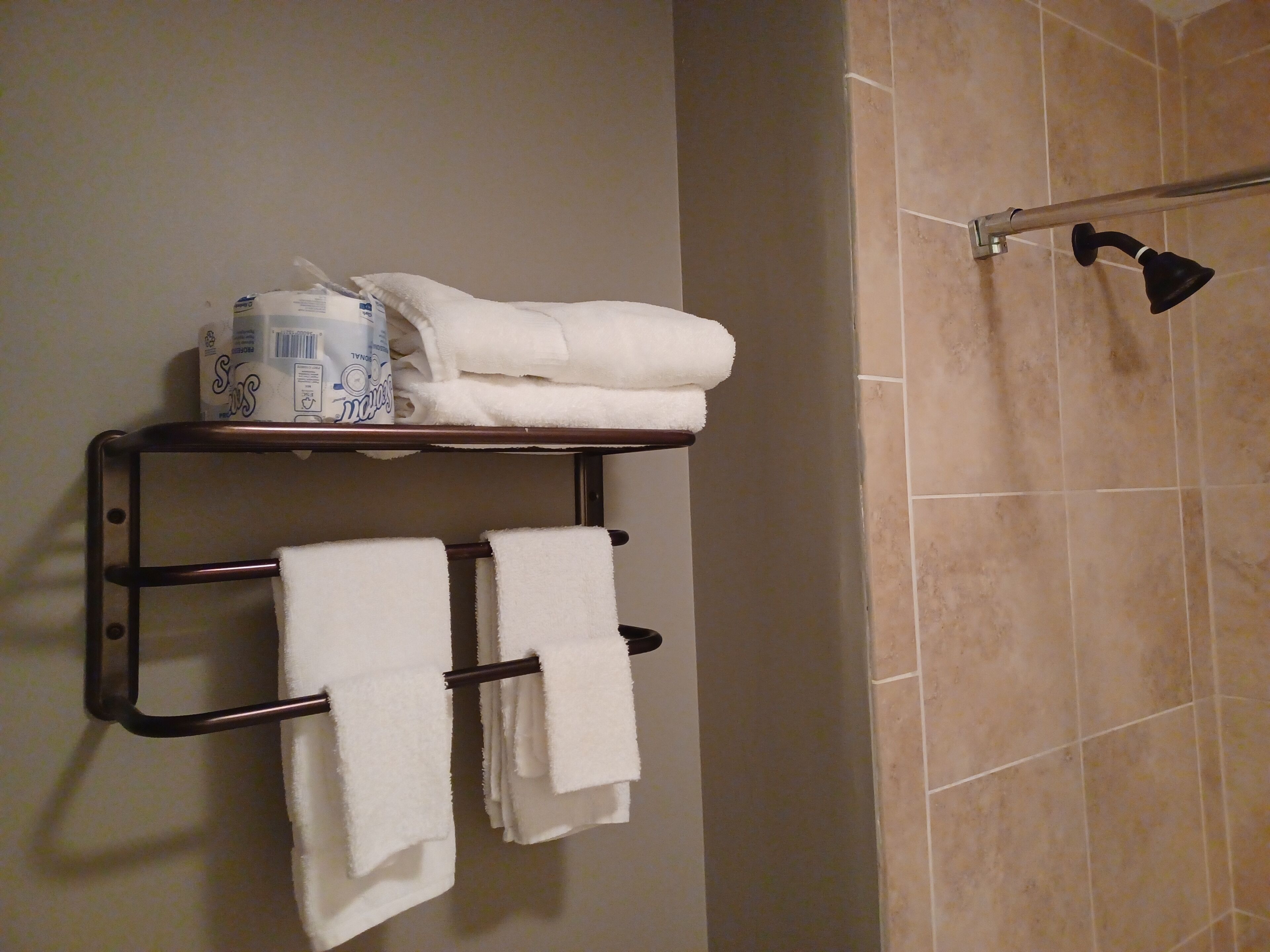 A bathroom with a towel rack holding two white towels and a stack of white towels on a shelf.