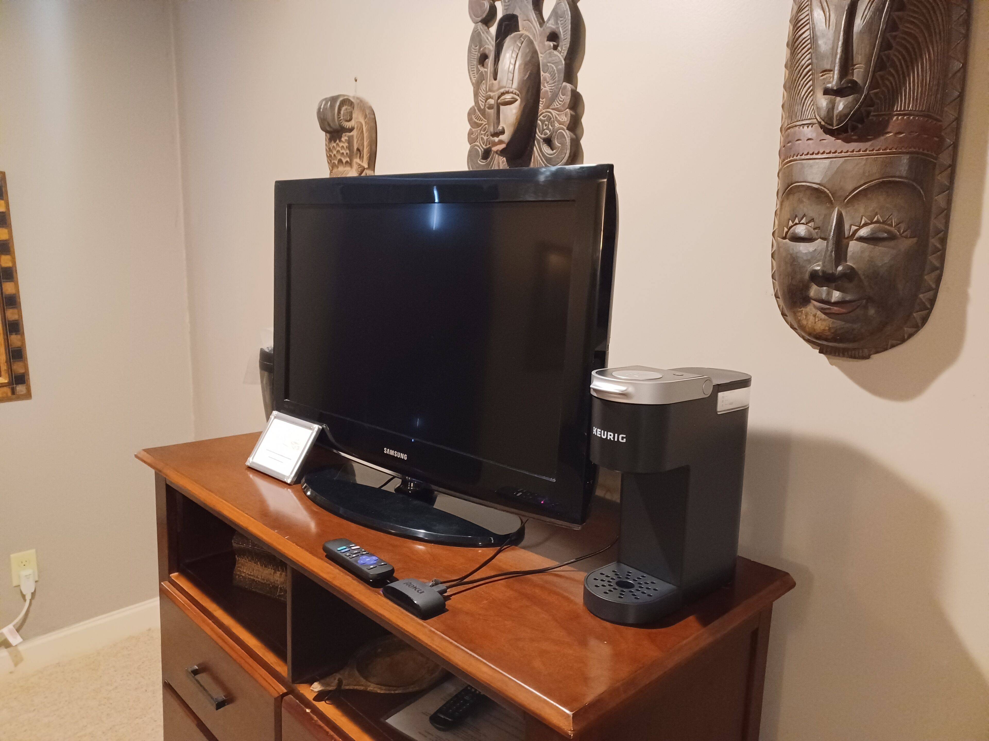 Een houten entertainmentcentrum met een Samsung tv, een Keurig koffiezetapparaat en een afstandsbediening.