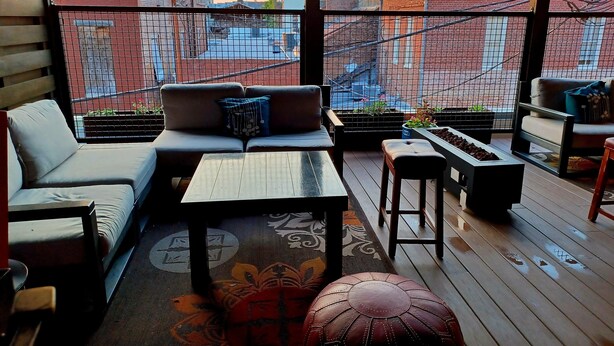 A balcony with a sofa, a small table, and a stool. There is a view of buildings and a sunset in the background. - Natchez Manor Bed & Breakfast (Natchez)