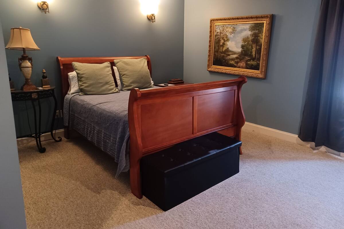 A bedroom with a wooden bed, a nightstand, a lamp, and a framed painting on the wall.