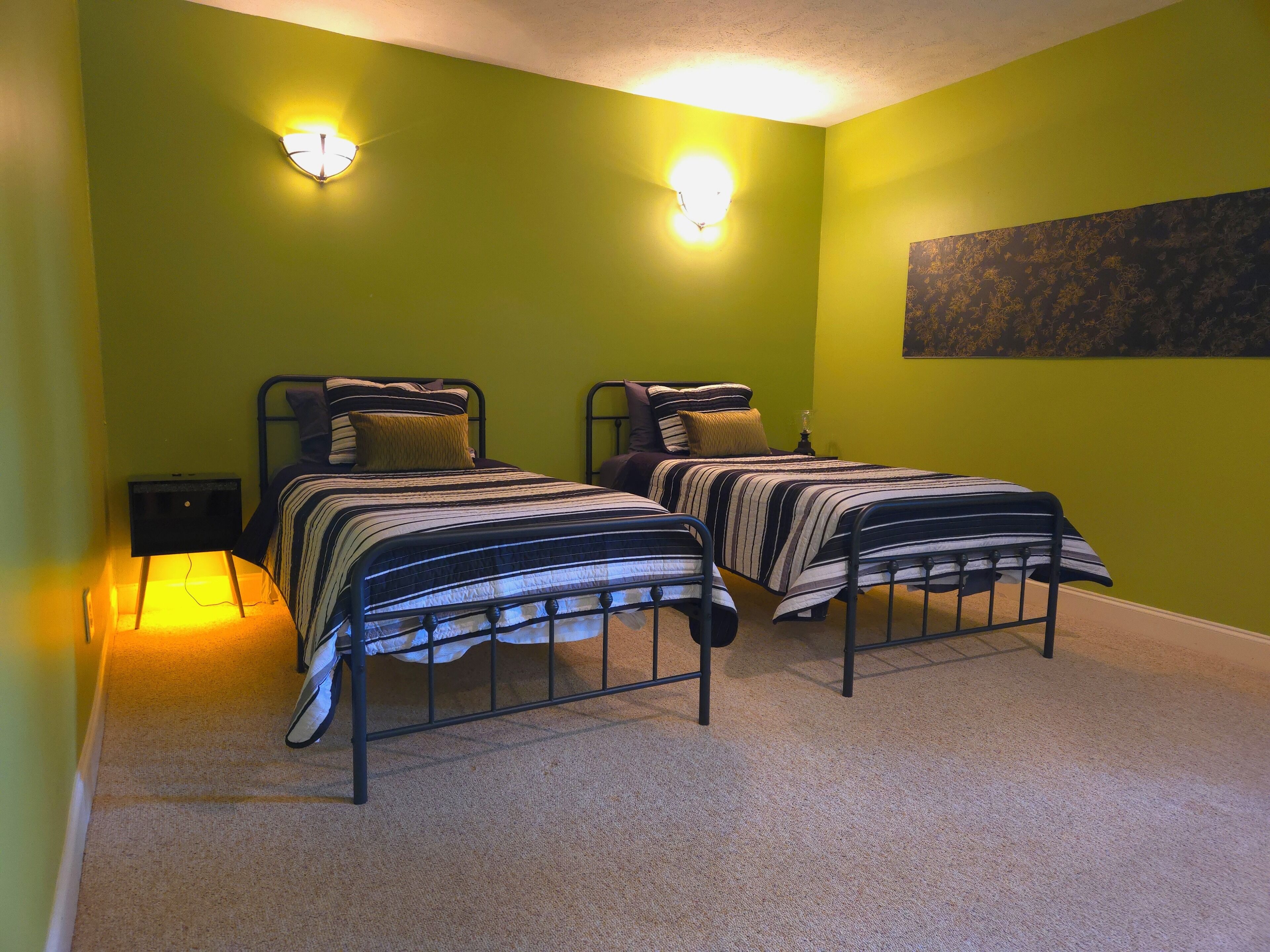 A room with two beds, green walls, and a painting.