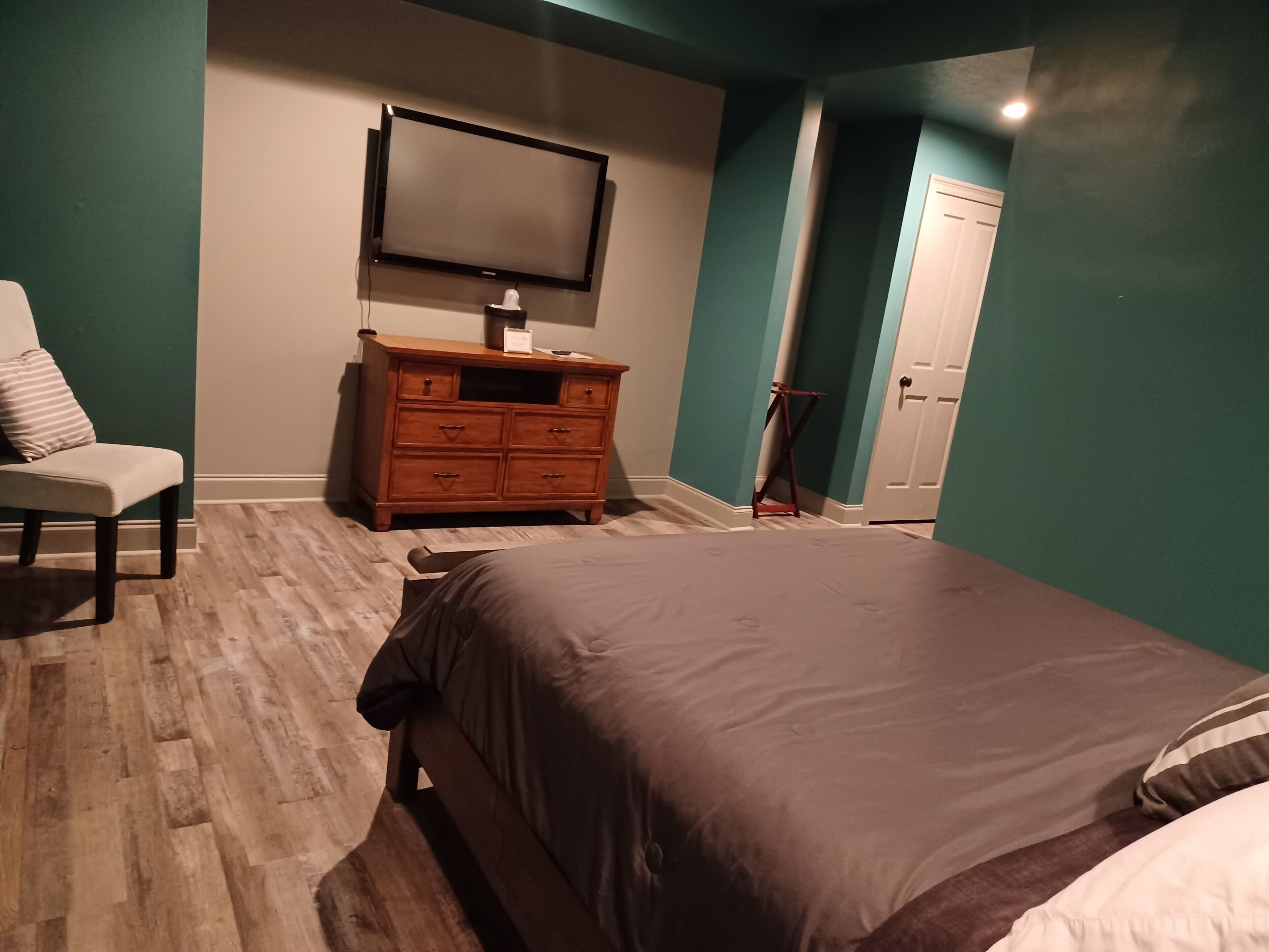 A bedroom with a bed, a dresser, a chair, a television, and a door.
