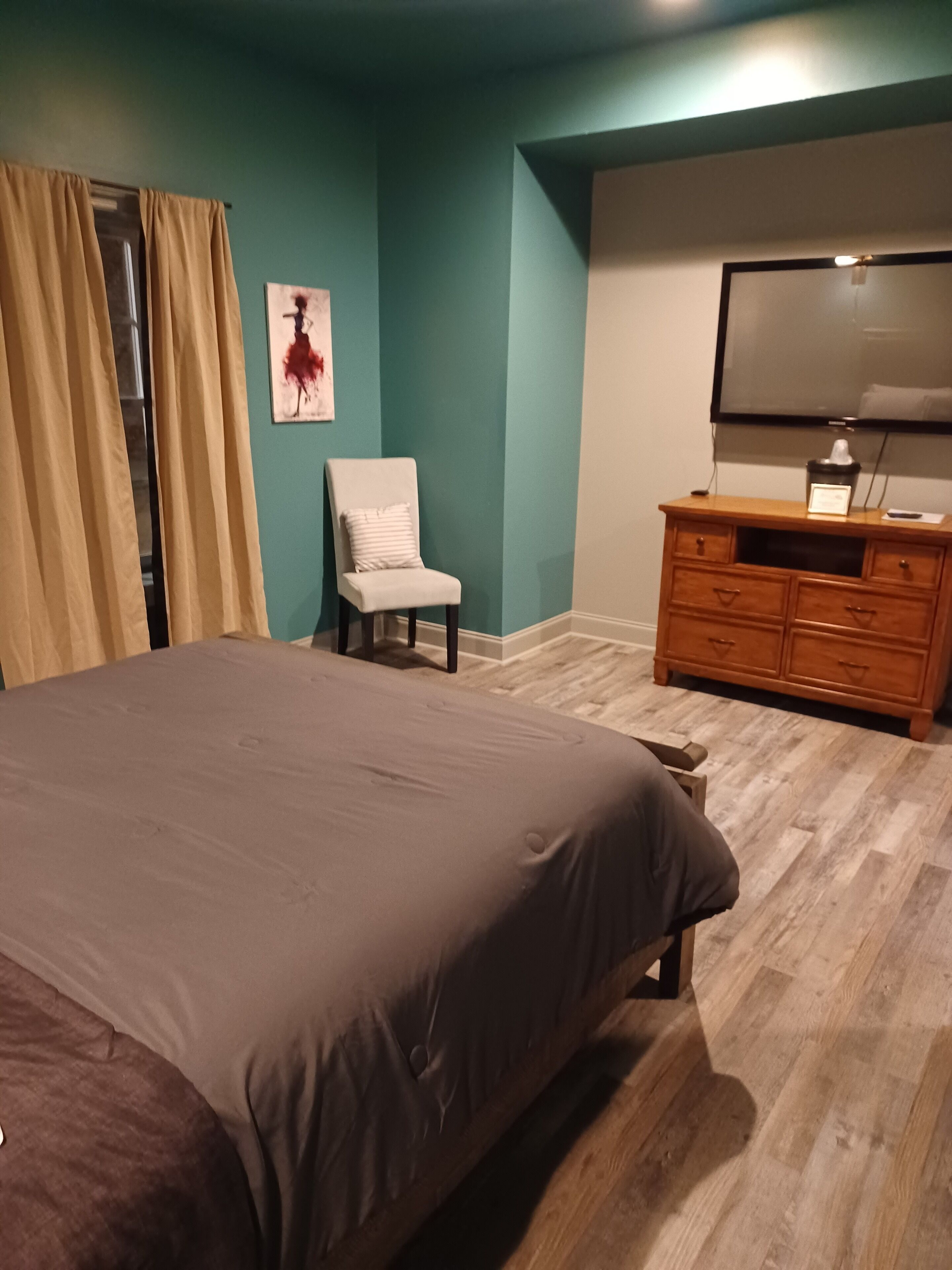 A bedroom with a bed, a chair, a dresser, and a TV.