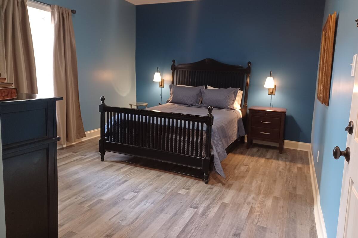 A bedroom with a wooden bed, two bedside tables, a dresser, and a window with curtains.