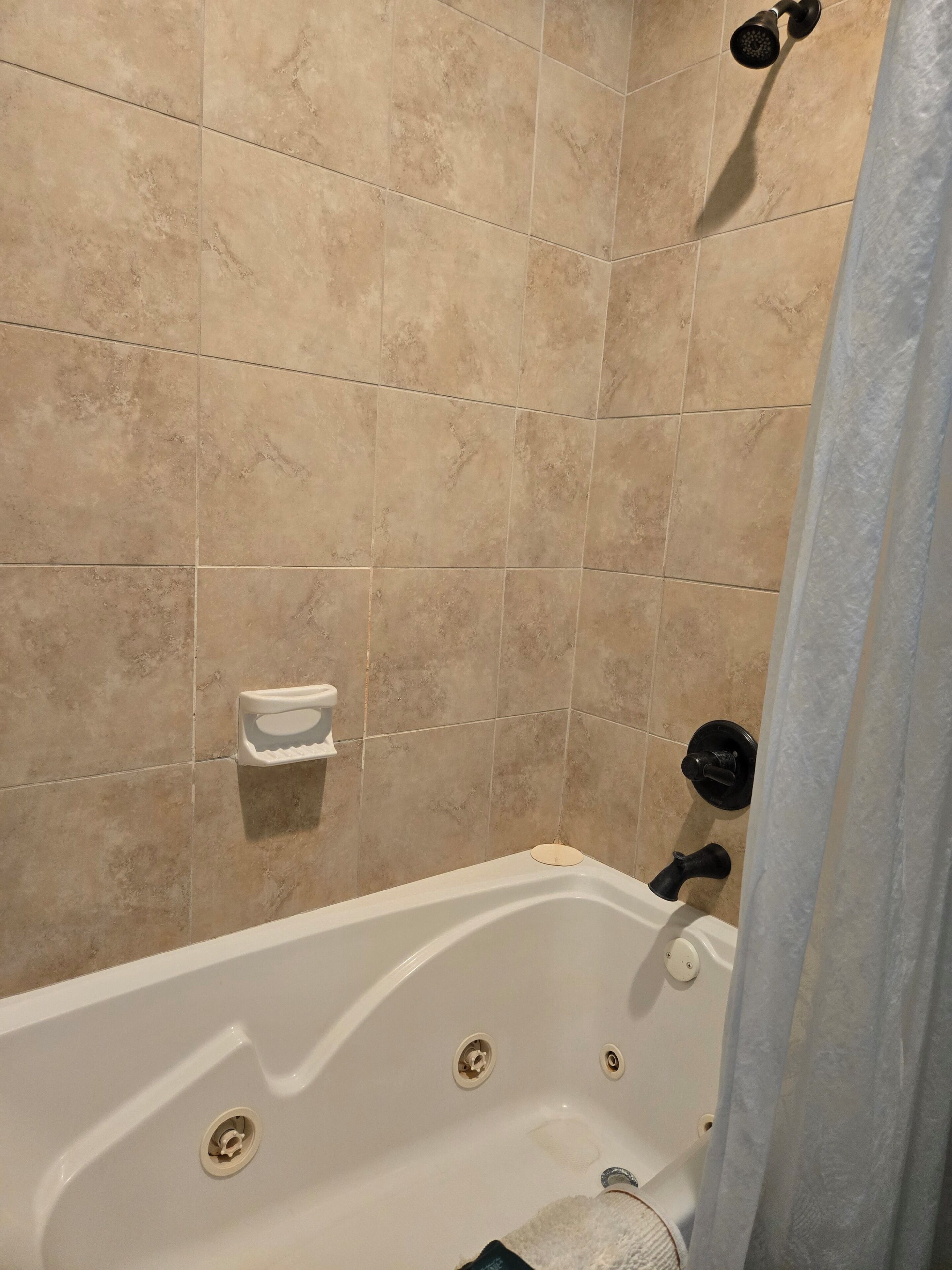 A bathroom with a bathtub, a showerhead, and a toilet paper holder on the wall.
