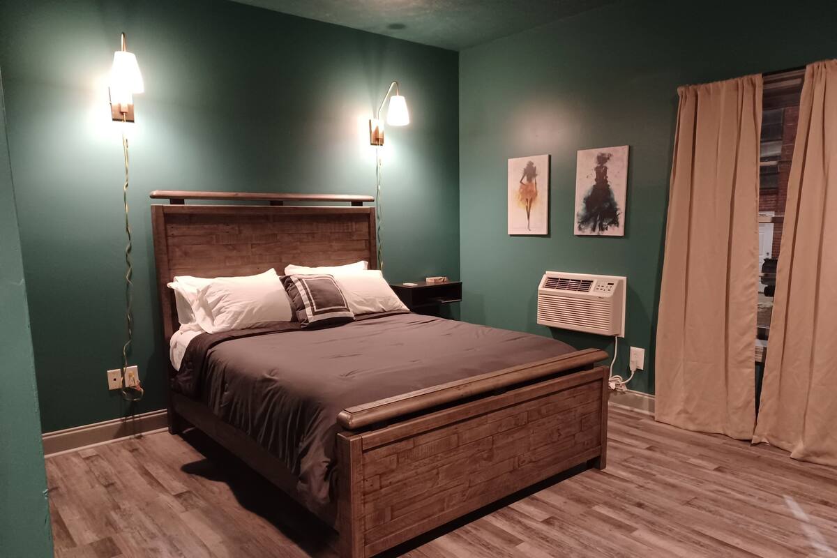 A bedroom with a wooden bed, two wall-mounted lights, a heater, and artwork on the wall.