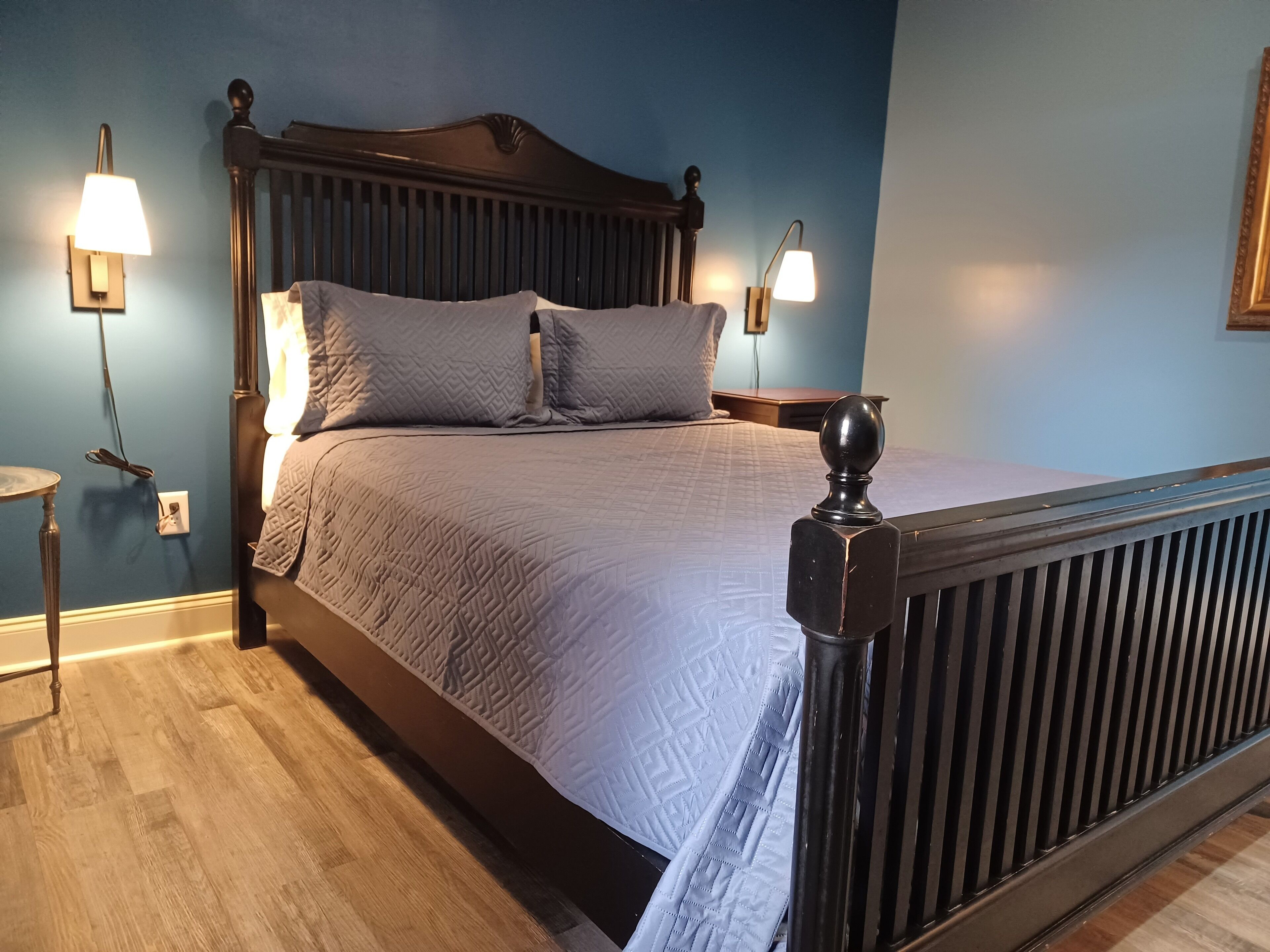 Una cama bien hecha con cabecera, dos lámparas de noche y una mesita redonda junto a la cama.