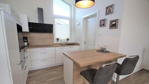 Une cuisine compacte avec des meubles blancs, un plan de travail en bois et un petit îlot central doté de tabourets de bar.