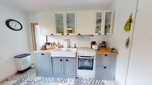 Une cuisine de taille réduite, avec des meubles blancs, un évier, une cuisinière et une horloge au mur.