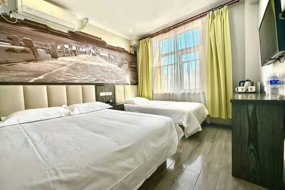 A hotel room with two beds, a wooden headboard, a large window with curtains, a desk with a mirror, and a television.
