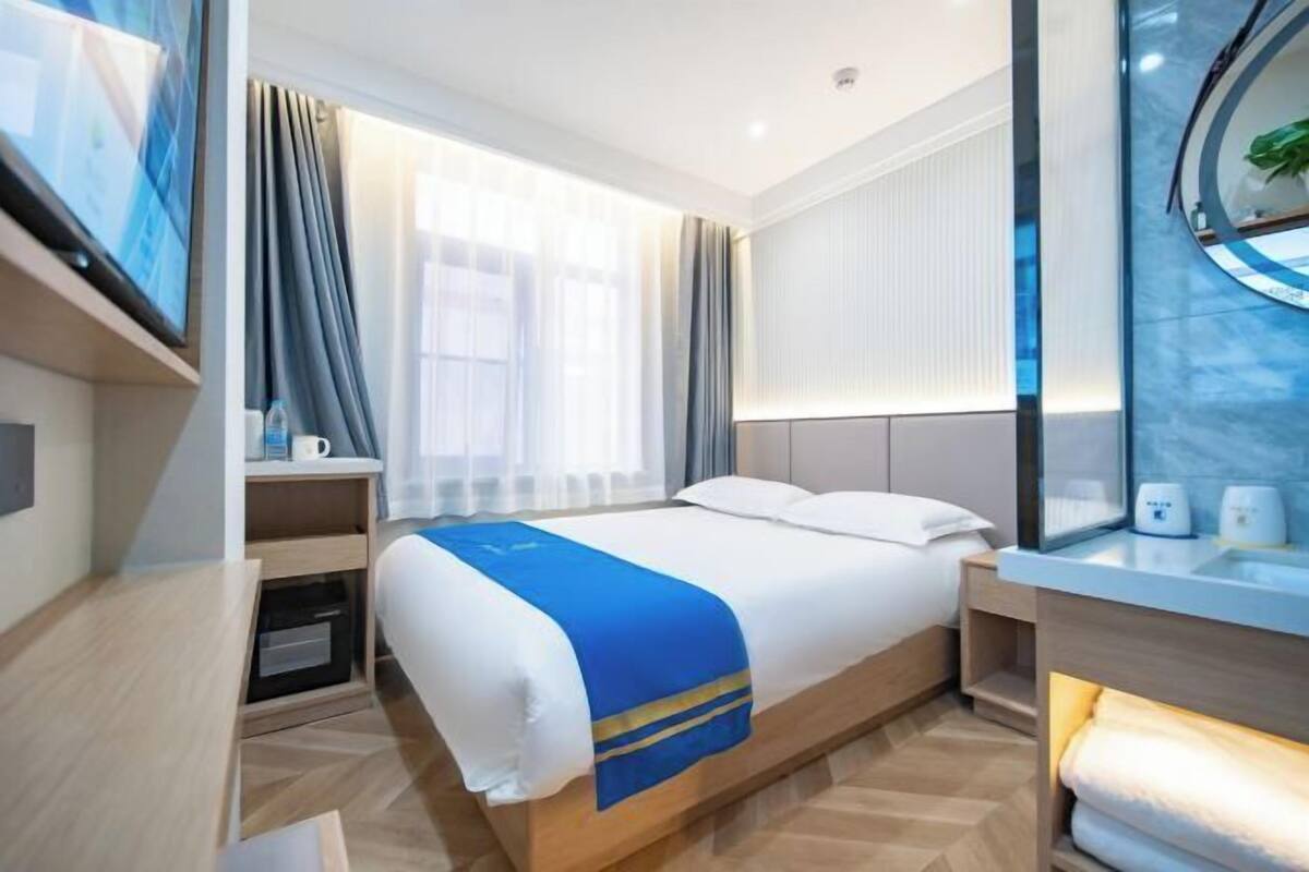 A modern hotel room with a large bed, bedside tables, a desk, and a window with curtains.