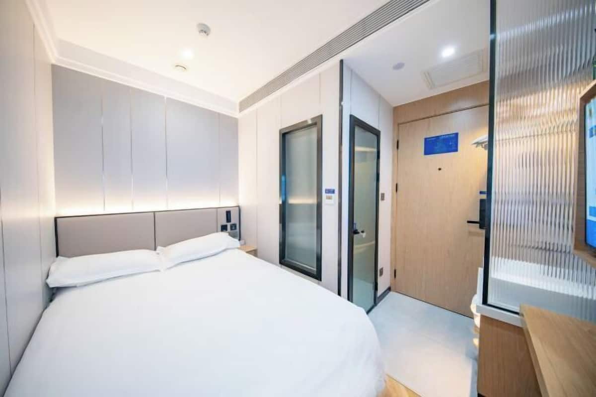 A modern hotel room with a large bed, a glass door closet, and a wooden desk.