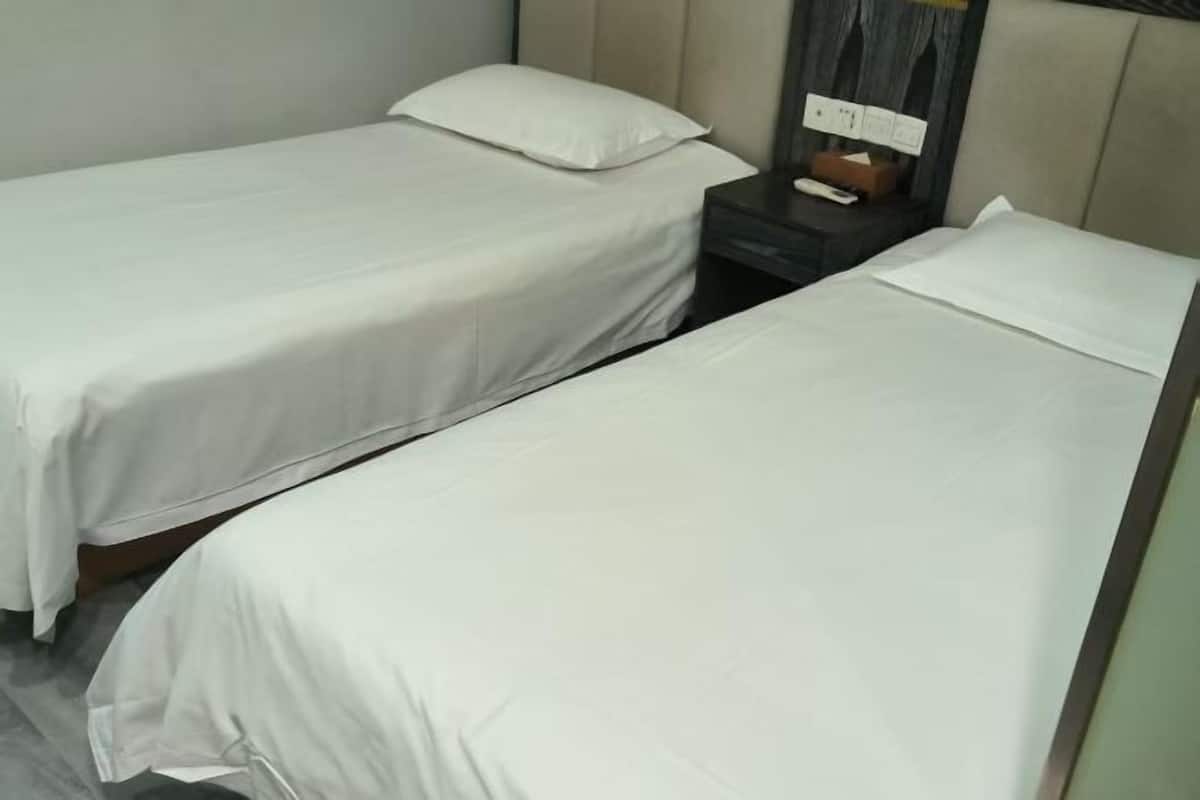Two single beds with white linens, a nightstand with a phone and a box, and a wall-mounted power outlet.