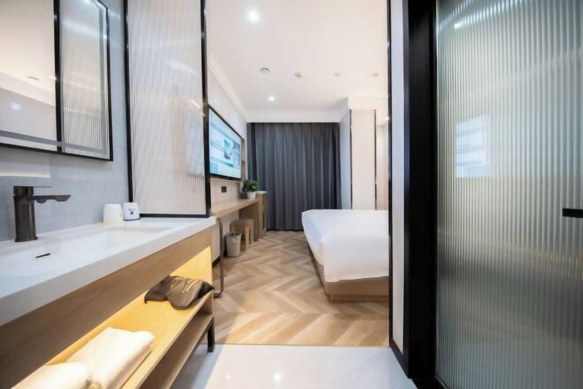 A modern hotel room with a large bed, a bathroom with a sink and mirror, and a television.